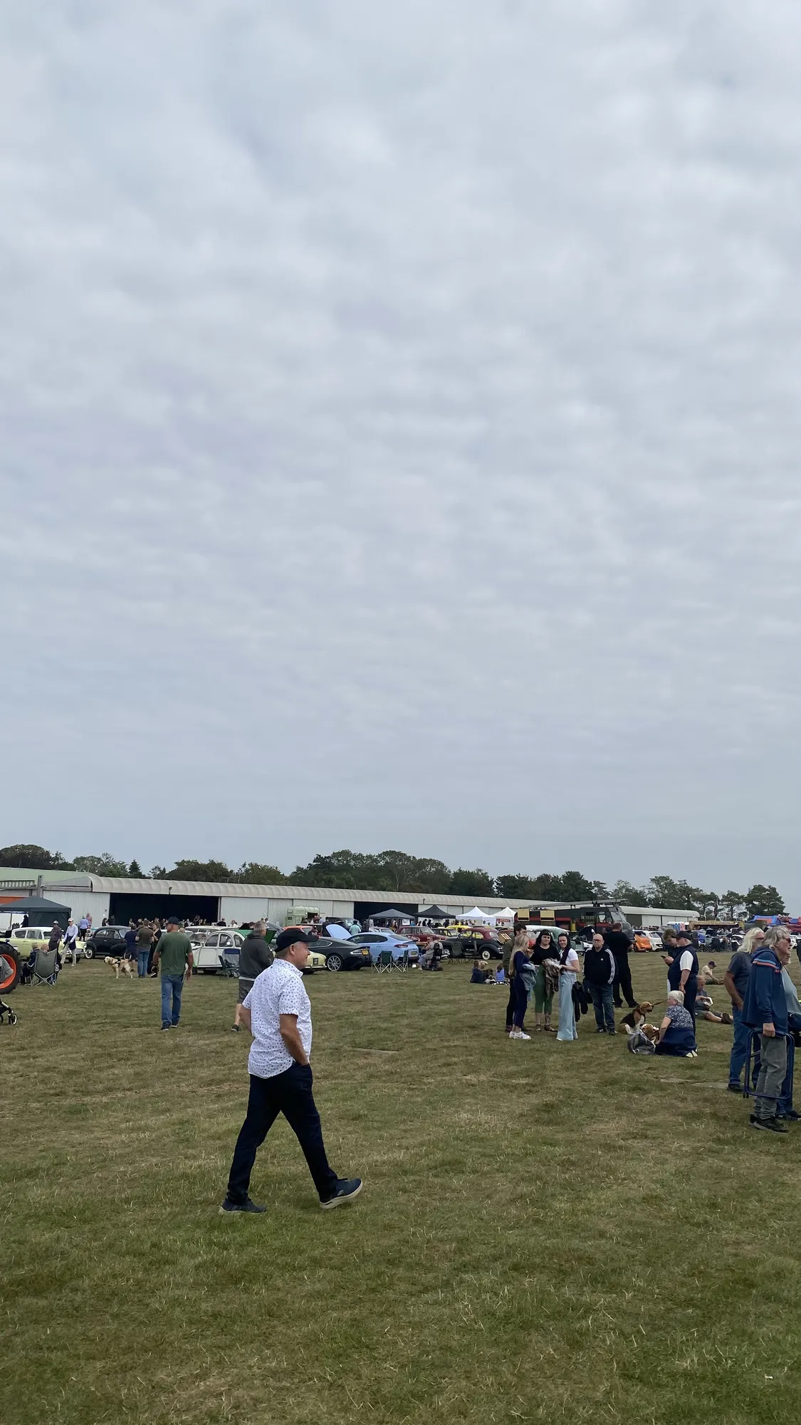 Visitors walking and sitting out on the open grass showground at Fenland Airfield, with no shade or shelter
