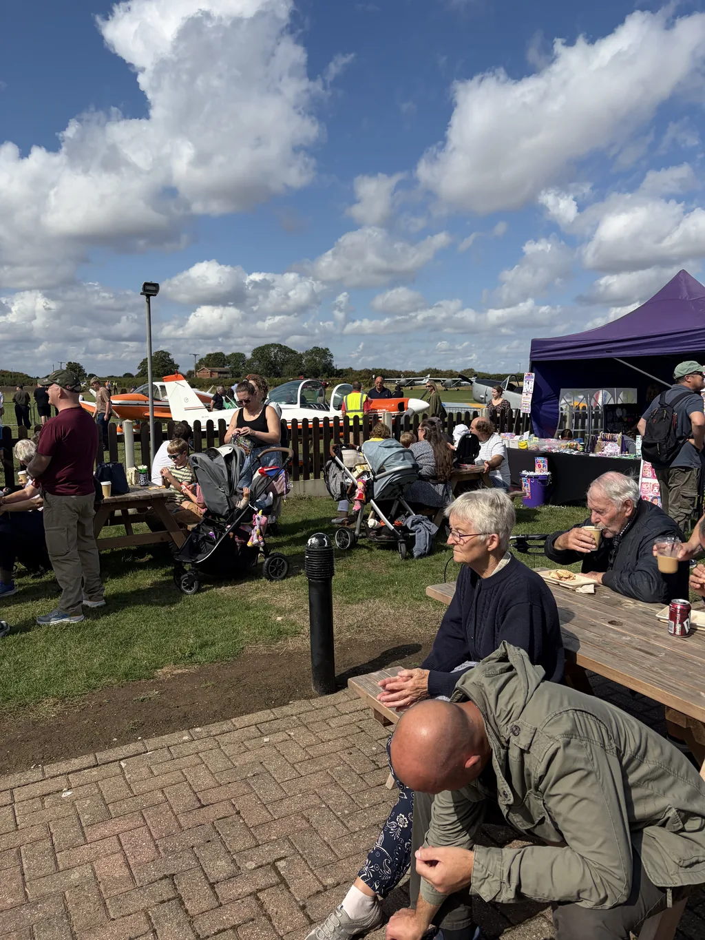 Visitors eating outside the clubhouse with aircraft parked beyond the fence