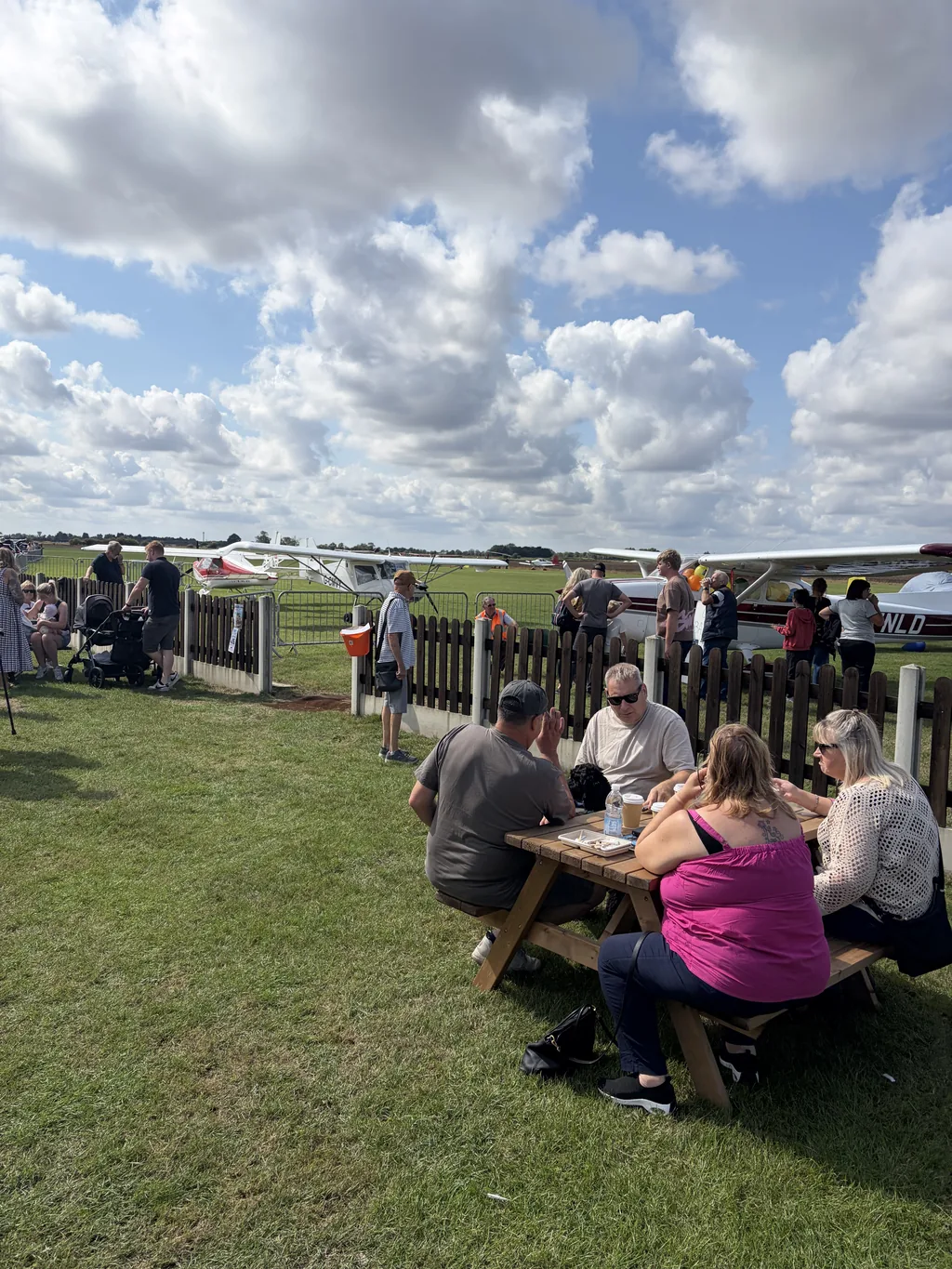 Visitors sitting at picnic tables beside the line of visiting aircraft